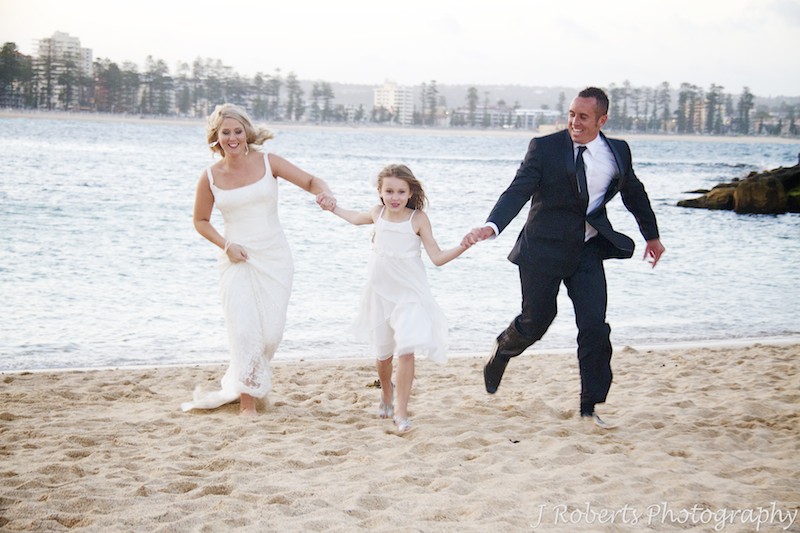 Bride and groom running up the beach with their daughter - wedding photography sydney